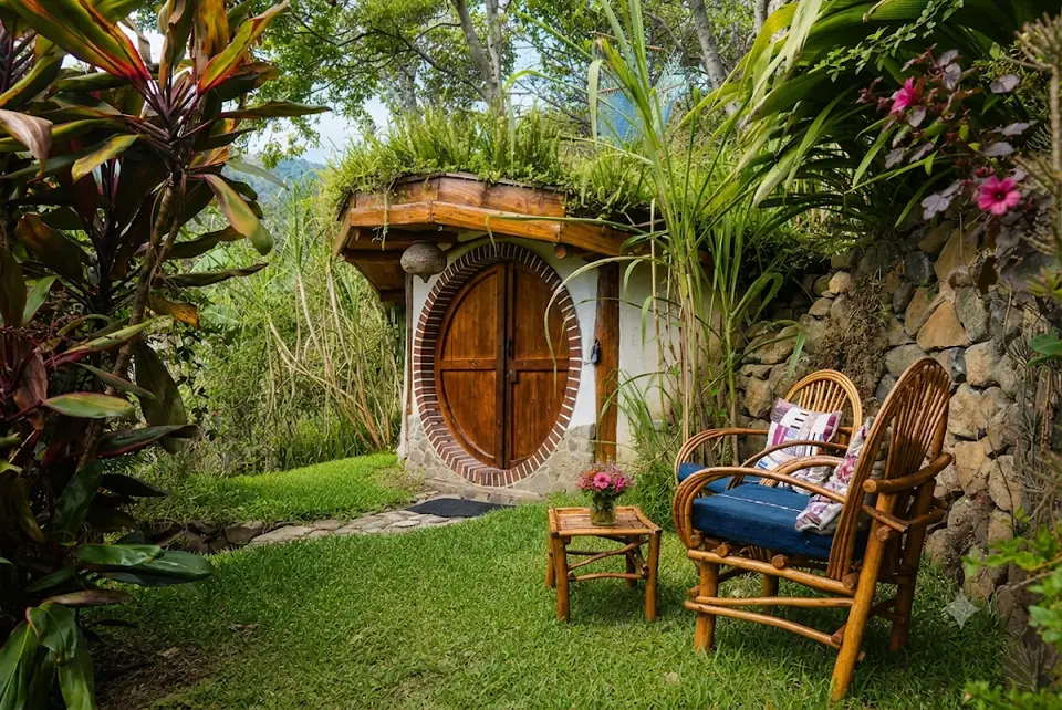 Hobbit House: exterior: round wooden door in the earthen hill, garden chairs.